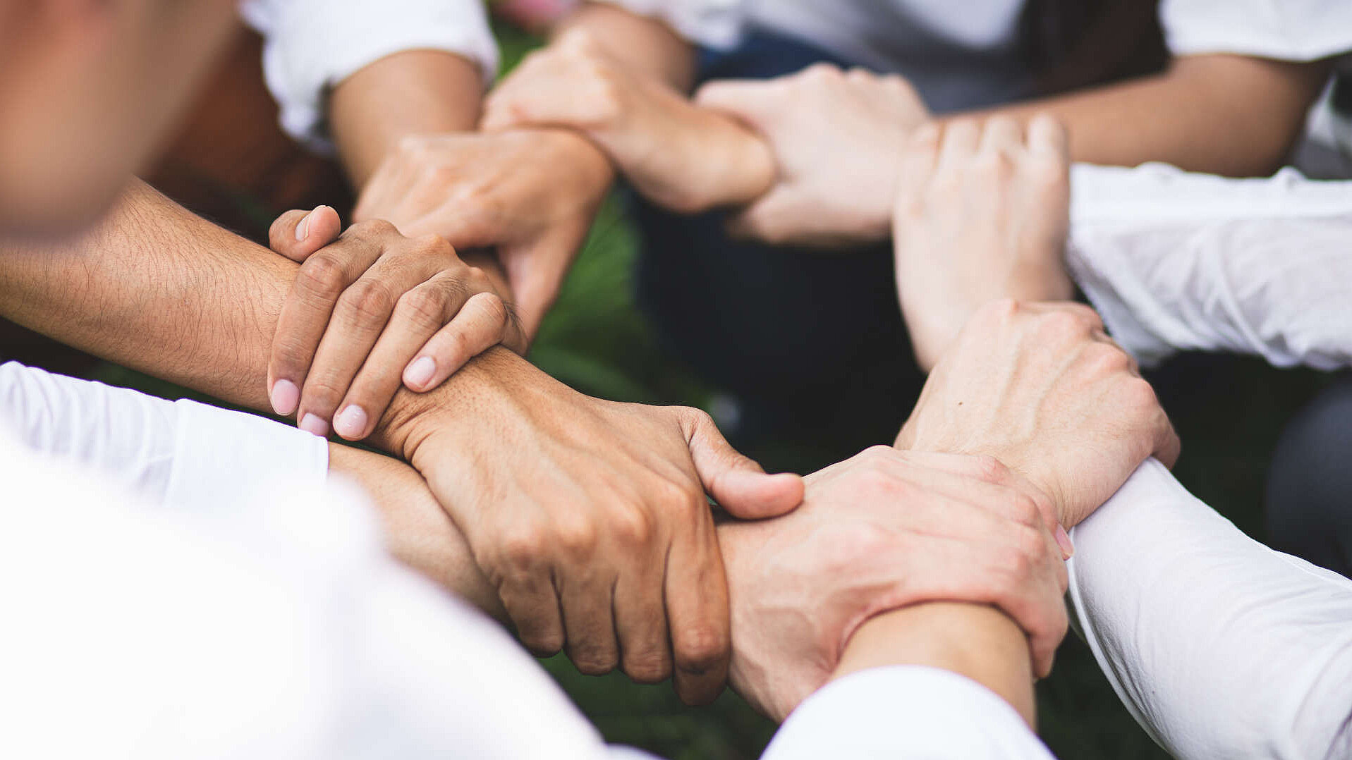 Nahaufnahme von mehreren übereinanderliegenden Händen, die sich gegenseitig halten als Symbol für Demokratie
