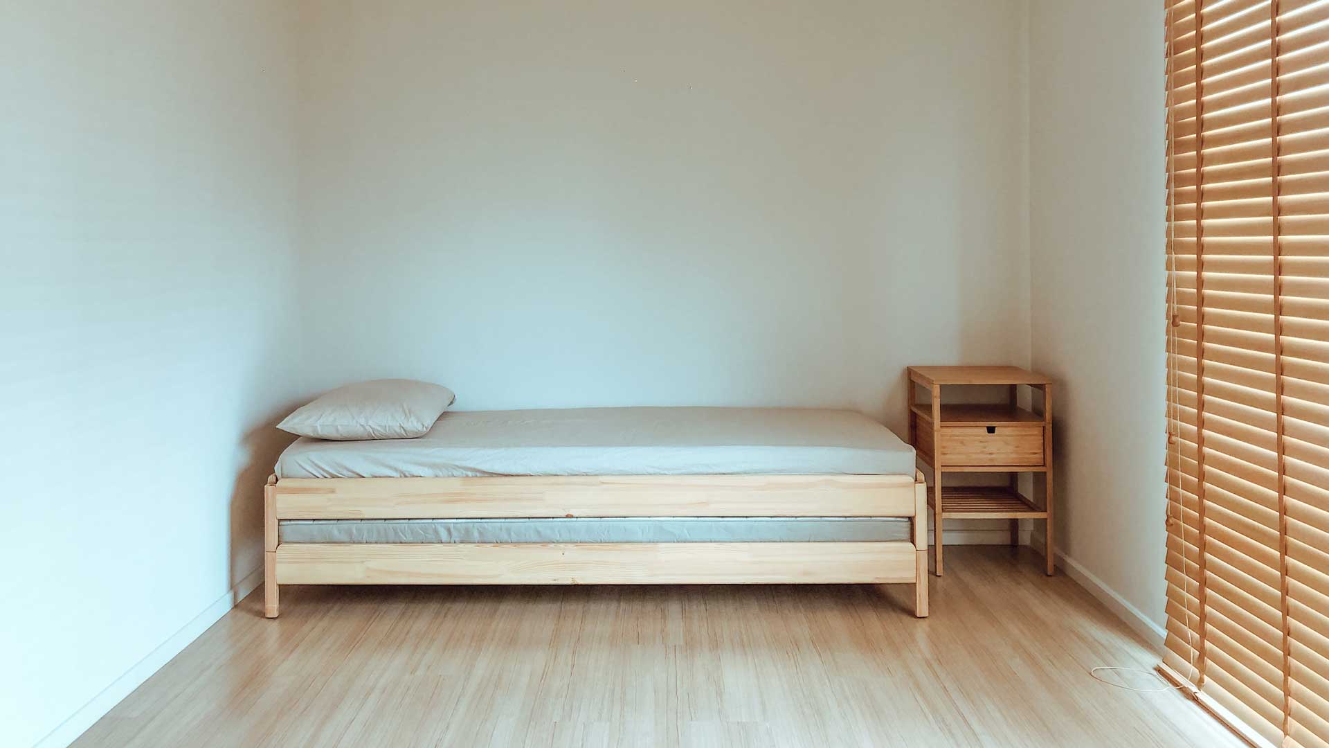 Blick in ein Zimmer mit Bett, Matratze, Kissen und kleinem Holzmöbel.