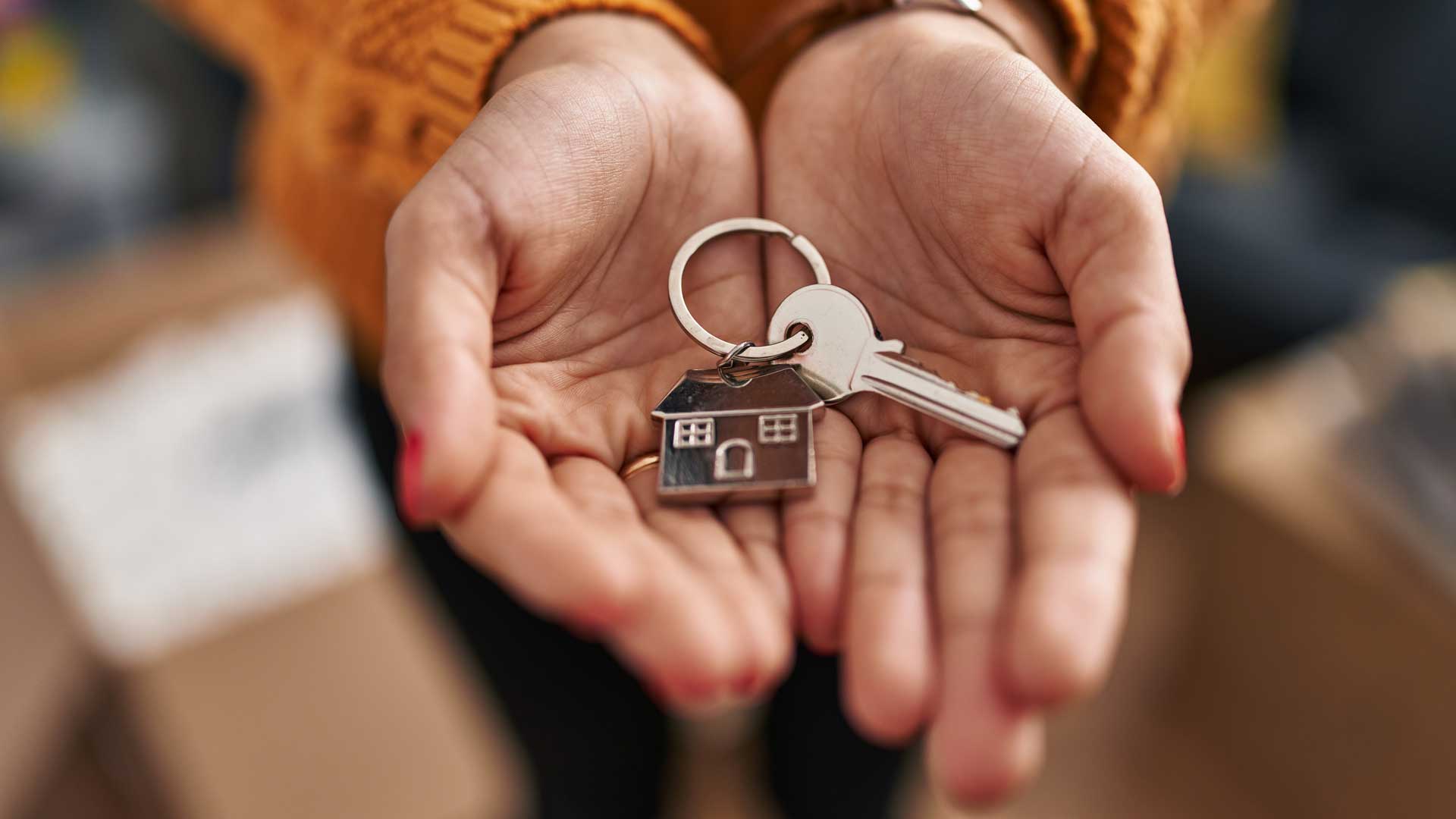 Zwei offene Hände halten einen Schlüsselbund mit Hausschlüssel und Haus-Anhänger.
